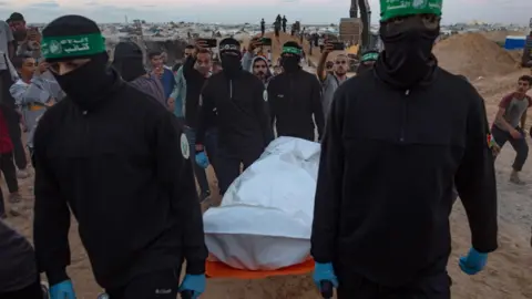 EPA Members of Hamas's armed wing carry a white bag containing what they said was the body of a hostage after retrieving it from an underground tunnel in Khan Younis, southern Gaza (28 October 2025)