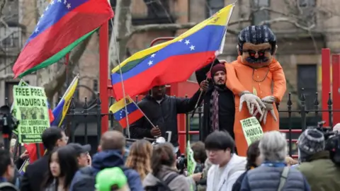 Reuters Protesters demonstrate in support of ousted Venezuelan President Nicolas Maduro, many waving Venezuelan flags and 'Free Maduro' signs. A man also holds up a large stuffed maquette of Maduro in prison clothes and chains