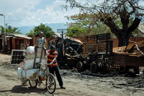 AFP A displaced man accompanied by his child, returns from Kigubhe where he had sought refuge, as he passes a charred military vehichle in Luvungi on December 13, 2025