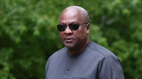 Anadolu via Getty Images John Mahama wearing sunglasses and dark grey clothes, walking on Downing Street.