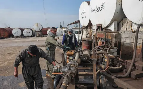 Sedat Suna / Gett Images Workers at a market for automotive fuel work on an industrial vehicle next to tanks of oil against a blue sky in Erbil, Iraq, on 17 March.
