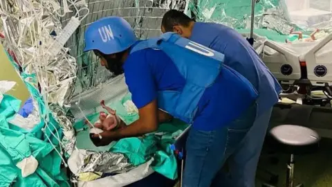 WHO Woman wearing blue UN helmet and bullet-proof vest holds a tiny baby
