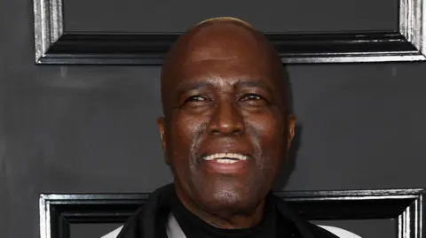 WireImage A close-up shot of Albert Mazibuko smiling with a black background behind him