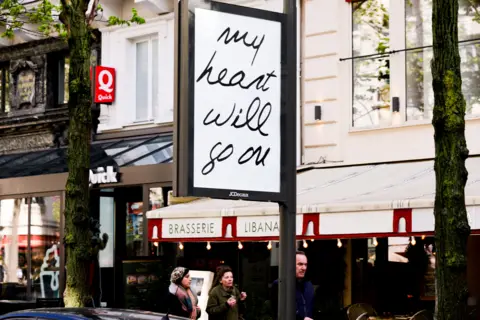 EPA A billboard reading "my heart will go on" is seen against the backdrop of a Parisian brasserie