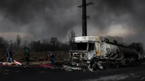 Reuters Firefighters surrounding a burnt out fuel tanker