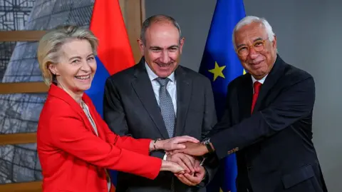 AFP via Getty Images A woman in a red jacket puts her hands on top of the hands of two men both in blue suits