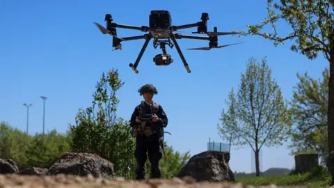 Getty Images A soldier from the US Army in full combat gear stands in the background piloting a drone in a simulated village during the Combined Resolve 