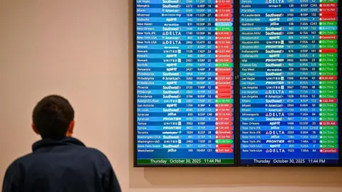 Getty Images A file photo of a man standing in front of a screen showing cancelled flights. 