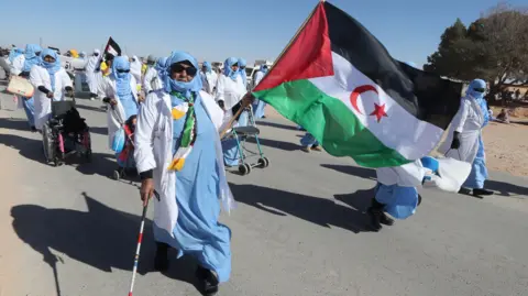 EPA An elderly woman in blue and white headscarf carries a Western Saharan flag ahead of other protestors