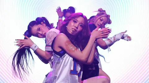 Getty Images The pop group XG dance in formation against a backdrop of concentric circles