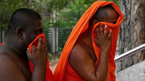 AFP via Getty Images Two monks, wearing traditional orange attire, try to conceal their faces as they walk up stone stairway outside a building which can't be seen