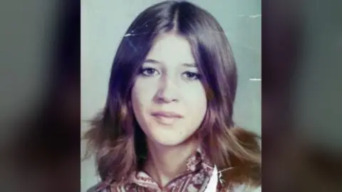 Police handout Laura Aimee, in a school photo from the 1970s. She has long brown hair parted down the middle and brown eyes, and wears a patterned blouse. 