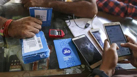 Getty Images A customer holds a SIM card packet while waiting to connect his mobile phone to the carrier Reliance Jio, the mobile network of Reliance Industries Ltd., at a mobile phone store in Mumbai, India, on Monday, Oct. 24, 2016. 