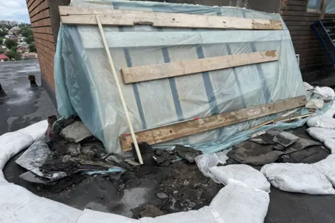 The site of a drone strike on a residential block roof covered with wood panels and blue plastic.