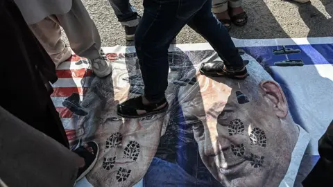 AFP via Getty Images A banner of Trump and Netanyahu laid out on the ground, being stomped by protesters.