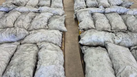 Australian Federal Police/Australian Border Force Large filled white bags, flecked with black, laid on the ground