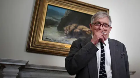 Getty Images David Hockney smoking in an art gallery in 2011. He is standing in front of an old master painting while doing so.