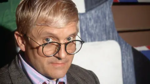 Getty Images David Hockney is seen looking to camera in a head and shoulders shot. He is peering over his round glasses and has his eyebrows raised.