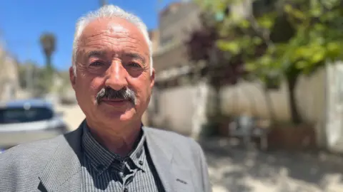 Fakhri Abu Diab, a middle-aged man with moustache, looks at the camera in a street in Jerusalem.