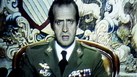 Getty Images King Juan Carlos wearing green military uniform, white shirt and black tie, sits with mouth open during his address of 23 February 1981.