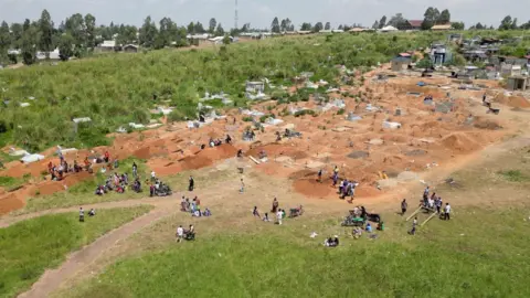 An aerial view of a graveyard in Bunia showing lots of fresh graves and groups attending burials