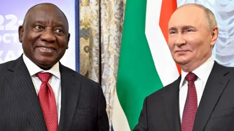 AFP via Getty Images South African President Cyril Ramaphosa (L) in pinstriped dark grey suit and red tie next to Russian counterpart Vladimir Putin in grey suit and similar tie. Behind them can be seen part of the South African flag.