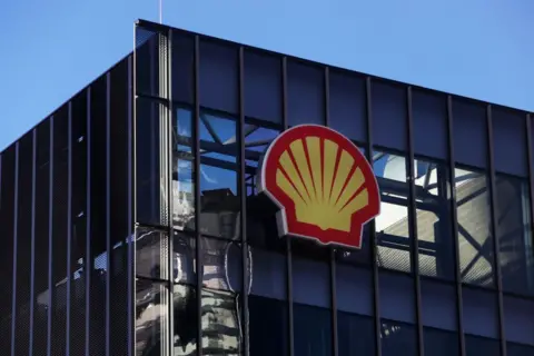 Getty The yellow and red shell logo of the company Shell on the side of a building with bright blue sky behind
