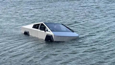 Grapevine Police Department A silver Tesla Cybertruck seen partially submerged in water, which has risen half way up the wheels, in a lake.