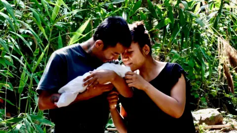 BBC/Darren Conway A couple hold a newborn baby in the arms, standing in front of the green of the jungle