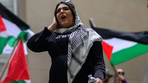 Getty Images Nerdeen Kiswani speaks during a protest commemorating Nakba Day on May 15, 2025 in the Brooklyn borough of New York City as Palestinian flags wave behind her.