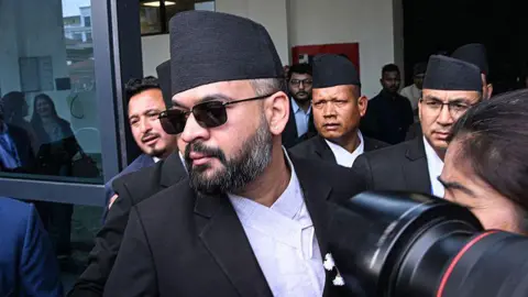 AFP via Getty Images Balendra Shah walking through a door, swarmed by the media and surrounded by other men in suits