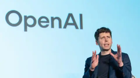 Getty Images Open AI CEO Sam Altman speaks during a talk session with SoftBank Group CEO Masayoshi Son at an event titled "Transforming Business through AI" in Tokyo, Japan - he has his hand held up and appears to be mid saying something, with the OpenAI logo on the wall behind him 