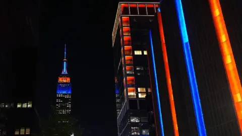 Anadolu via Getty Images City skyscrapers lit up in orange and blue amid night sky