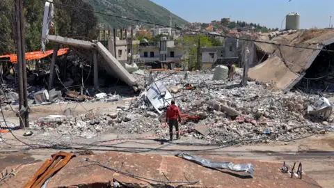 Neha Sharma/BBC A man stands next to a destroyed building in Lebanon