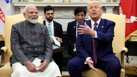 Reuters Modi, wearing a grey shirt, and Trump, in blue suit, sit on chairs in the White House