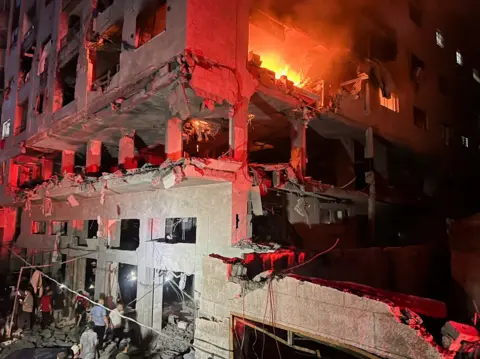 Reuters A fire burns in a residential building after Israeli shelling. People can be seen milling about below.