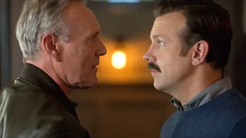Apple TV/Everett/Shutterstock Head facing and speaking to Jason Sudeikis in a scene from Ted Lasso 
