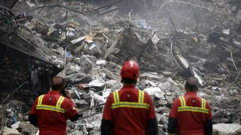 Getty Images Search and rescue officials stand before a site in Tehran heavily damaged by airstrikes