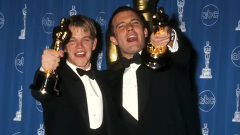 Getty Images US actors and screenwriters Matt Damon and Ben Affleck wear tuxedos and hold out the Oscar trophies they won for writing Good Will Hunting in 1998.