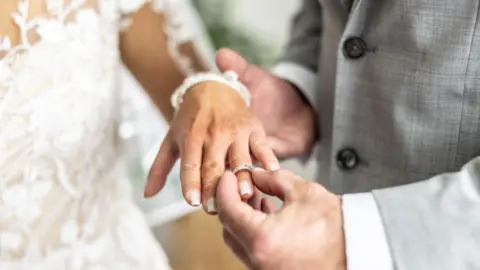 Getty Images A man puts a ring on a bride's finger