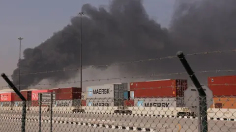 Reuters Smoke rises across the sky above shipping containers behind a fence