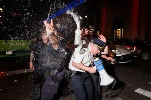 Getty Images NYPD officers duck as an open bottle of liquid is thrown towards them in New York City.