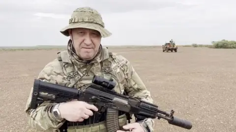 Getty Images Yevgeny Prigozhin, in military fatigues and a hat holding a weapon, in the desert.