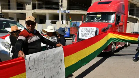 EPA Protesters hold a flag and sign next to a road block with several vehicles 