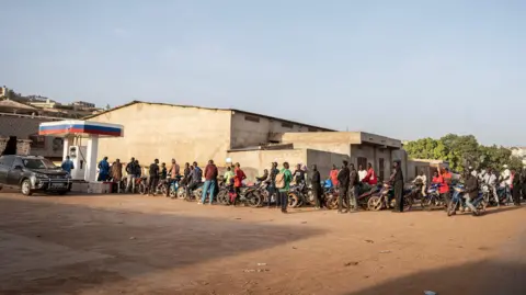 AFP via Getty Images Motorcyclists line up to get fuel at one of the few petrol stations with supply in Bamako on 10 December, 2025.