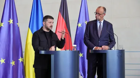 Getty Images German Chancellor Friedrich Merz and Ukrainian President Volodymyr Zelensky stand next to each other at podiums as they attend a joint press conference at the Chancellery following a virtual meeting hosted by Merz between European leaders and US President Donald Trump