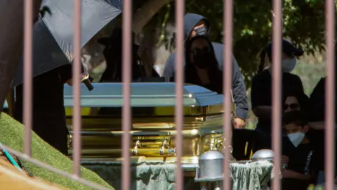 Reuters Mourners - some of them wearing surgical masks - look on as a gold-coloured casket containing the body of cartel leader Nemesio Oseguera Cervantes, known as 