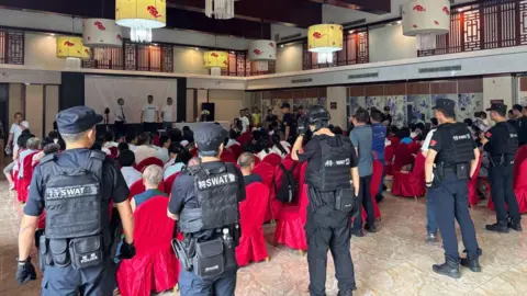 Early Rain Covenant Church SWAT officers surrounding congregants seated on red chairs in a ballroom