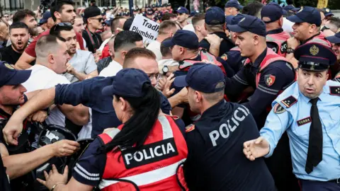Reuters A crowd of demonstrators clash with police during a protest. Officers in red and blue uniforms which say 'POLICIA' hold back male protesters.