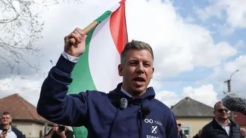 Jakub Porzycki/NurPhoto A man with a blue sweatshirt holds a Hungarian flag with green, white and red stripes